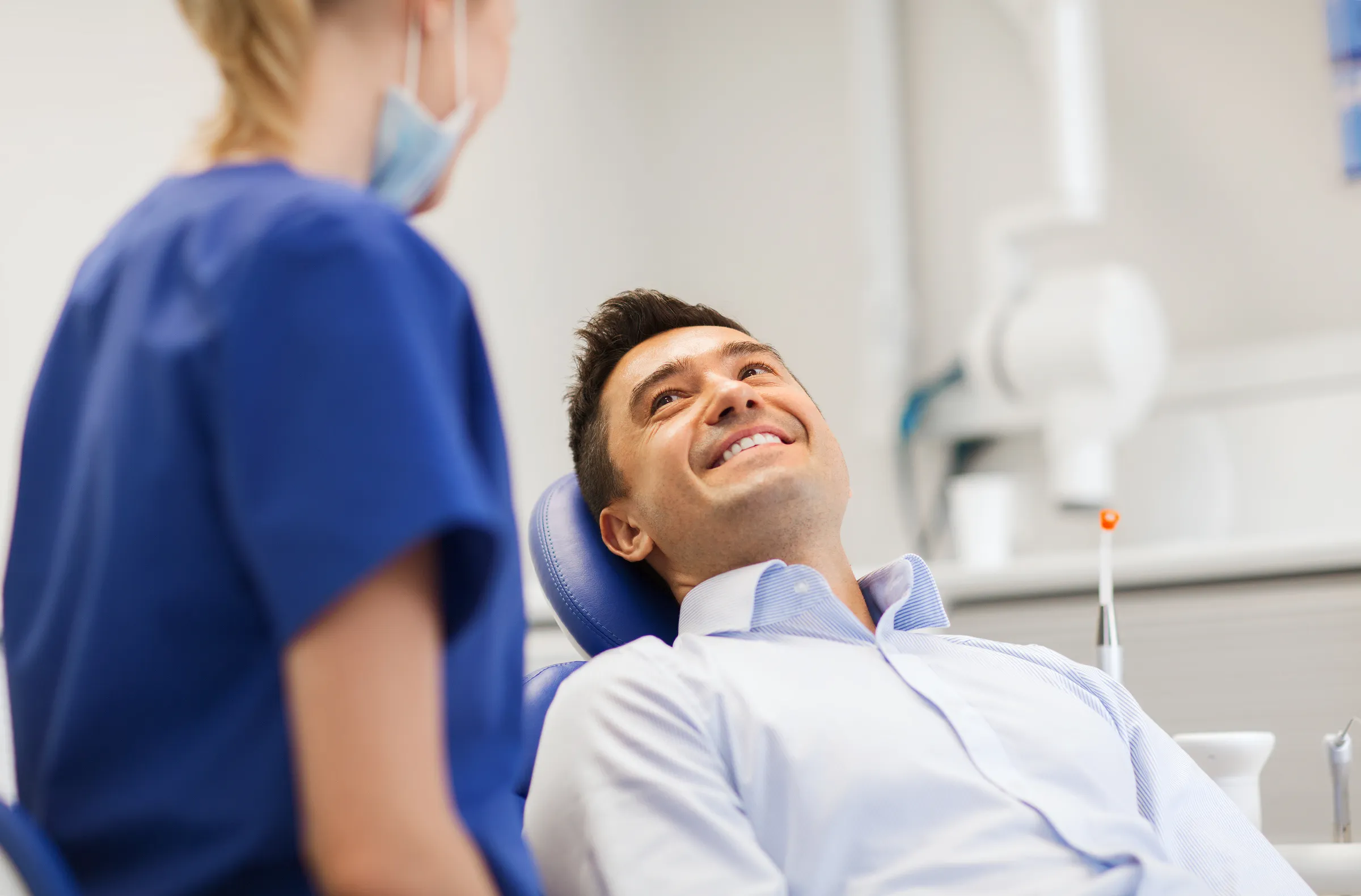 Smiling man in a dental chair talking with a dental assistant