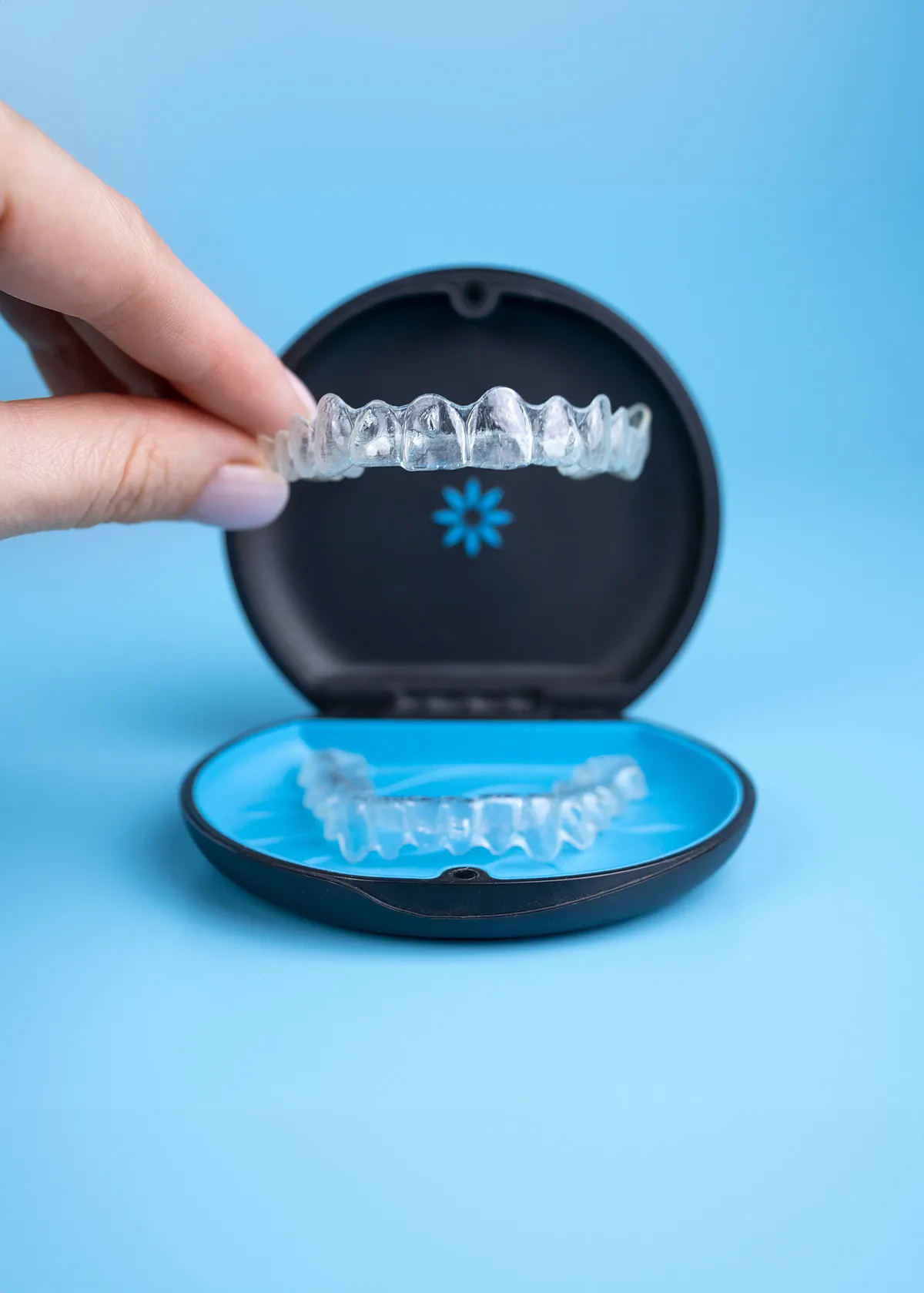 Hand lifting a clear aligner from its black storage case