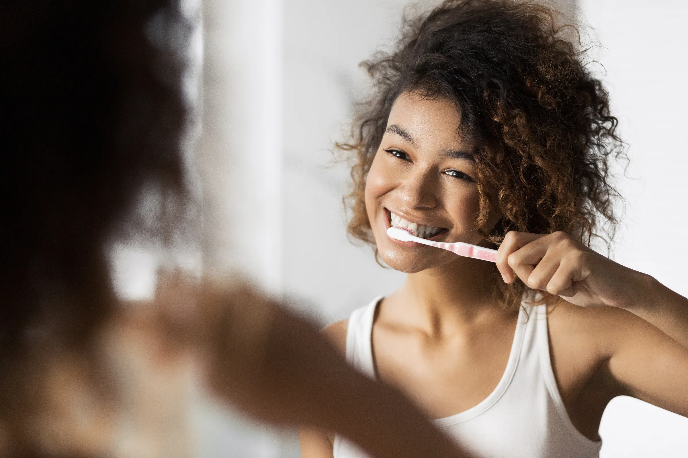 Smiling woman brushing her teeth in a mirror