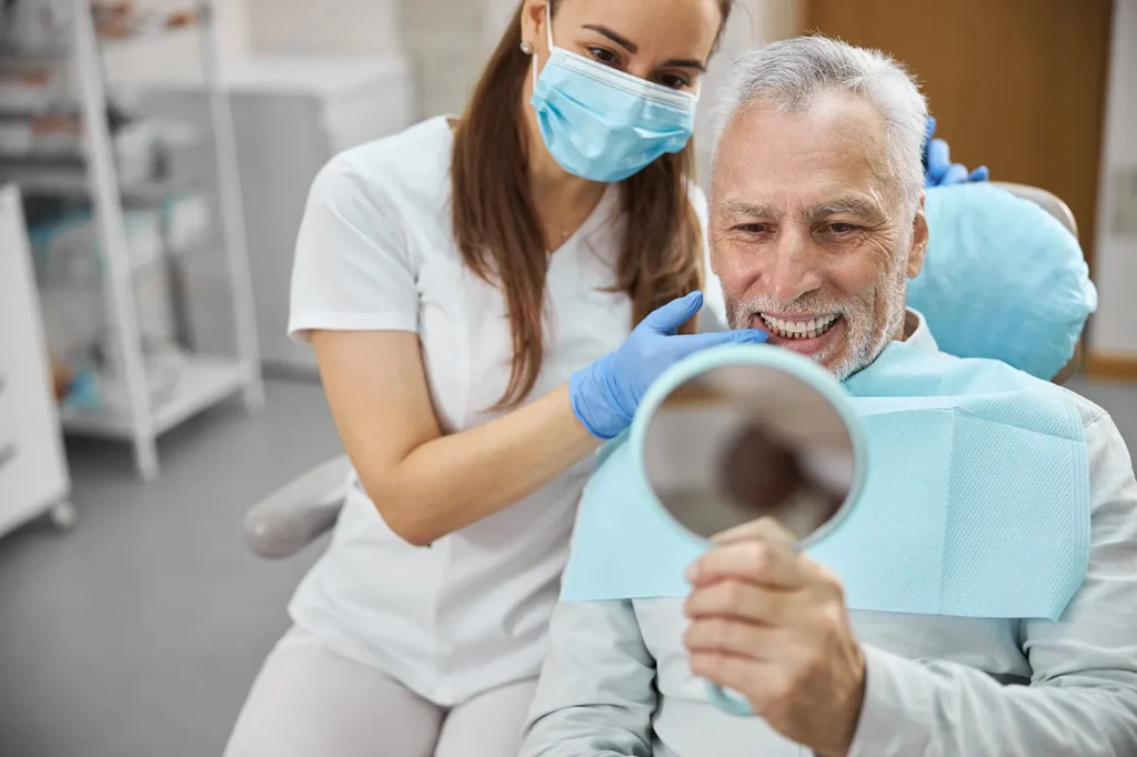 Older man checking his smile in a hand mirror with his dentist