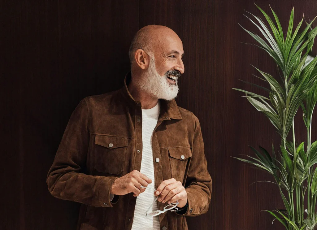 Smiling older man in a brown jacket beside a plant