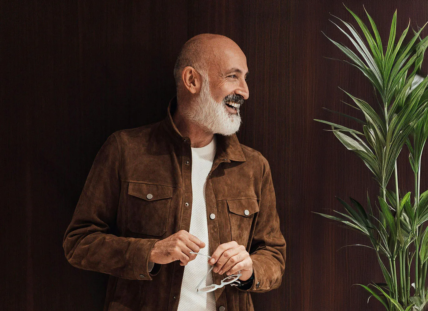 Smiling older man in a brown jacket beside a plant