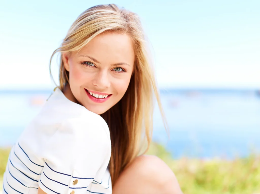 Smiling woman with long blond hair sitting by the ocean