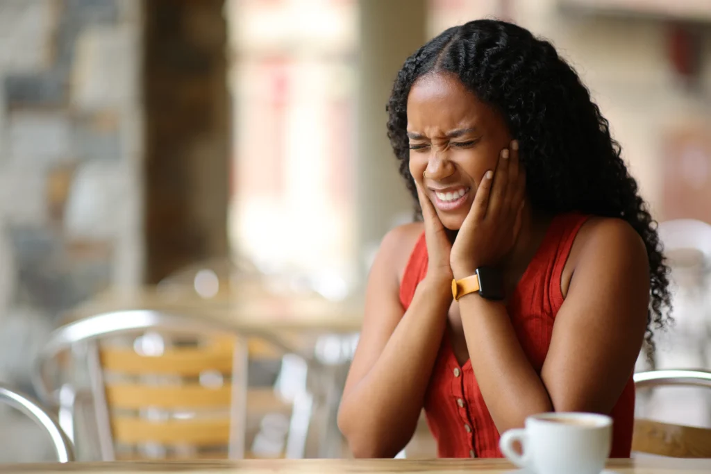 Woman holding both sides of her jaw in pain at a café table