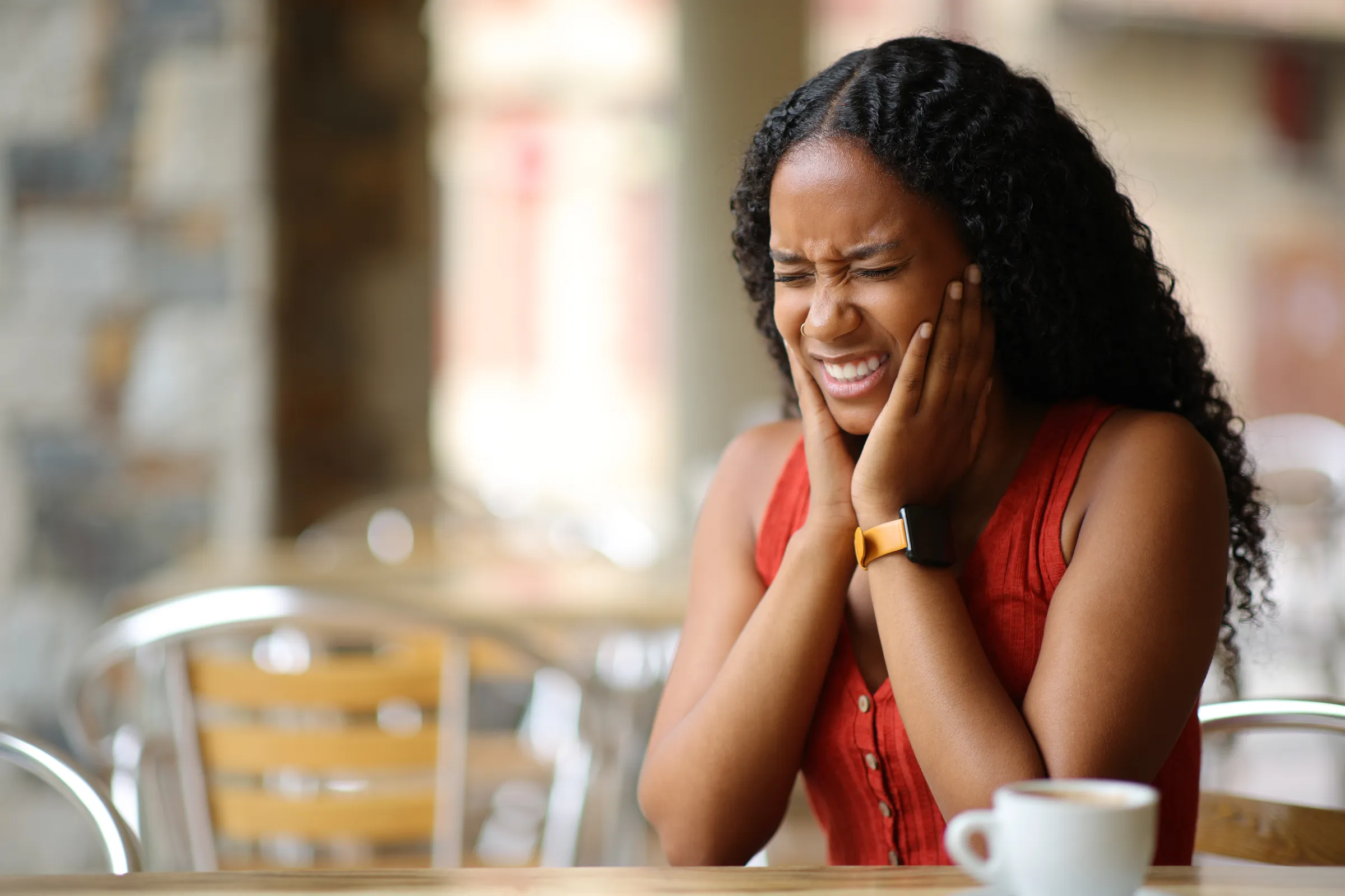 Woman holding both sides of her jaw in pain at a café table