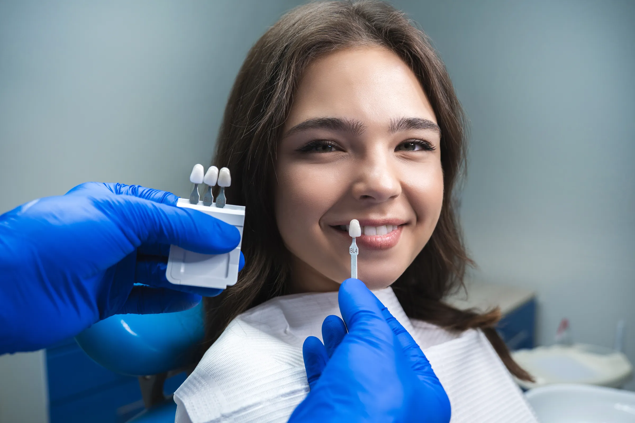 Dentist matching a shade guide to a smiling patient’s teeth