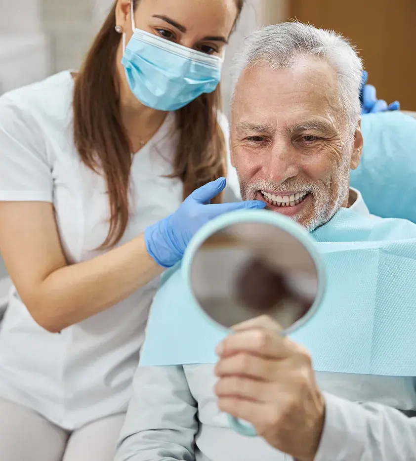 Older man checking his smile in a hand mirror with his dentist